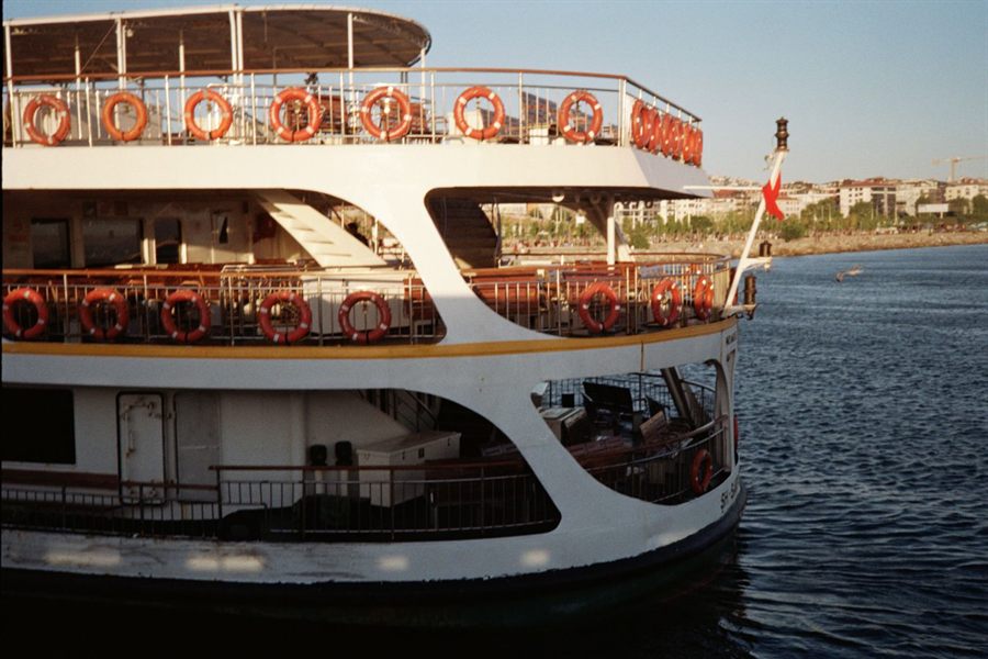 Stern of a docked river ship with red and white life rings along the rail